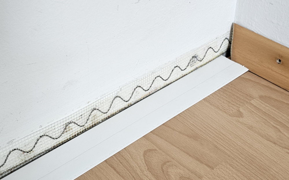 Installiertes iFOX-Heizband zur Schimmelschutz-Temperierung hinter der Sockelleiste – wellenförmig verlegtes Heizkabel mit Abdeckung, vorbereitet zur unauffälligen Montage